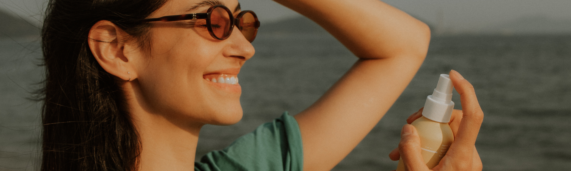 Femme appliquant la brume Sun Defense sur son visage sous le soleil, à la plage