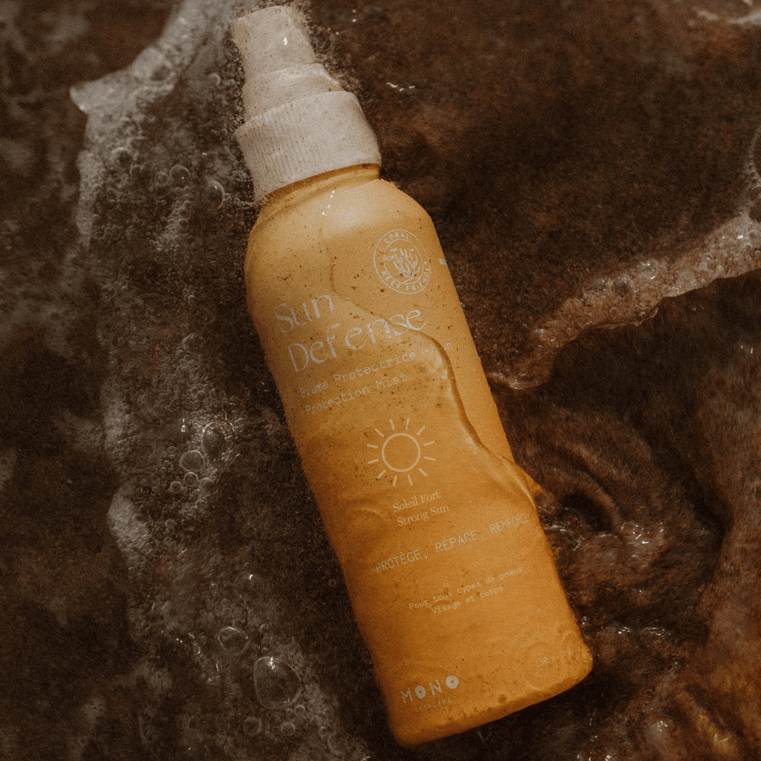 Bouteille en aluminium Mono Skincare posée sur le sable à la plage. Packaging solaire réutilisable et esthétique, pensé pour limiter l'impact environnemental.